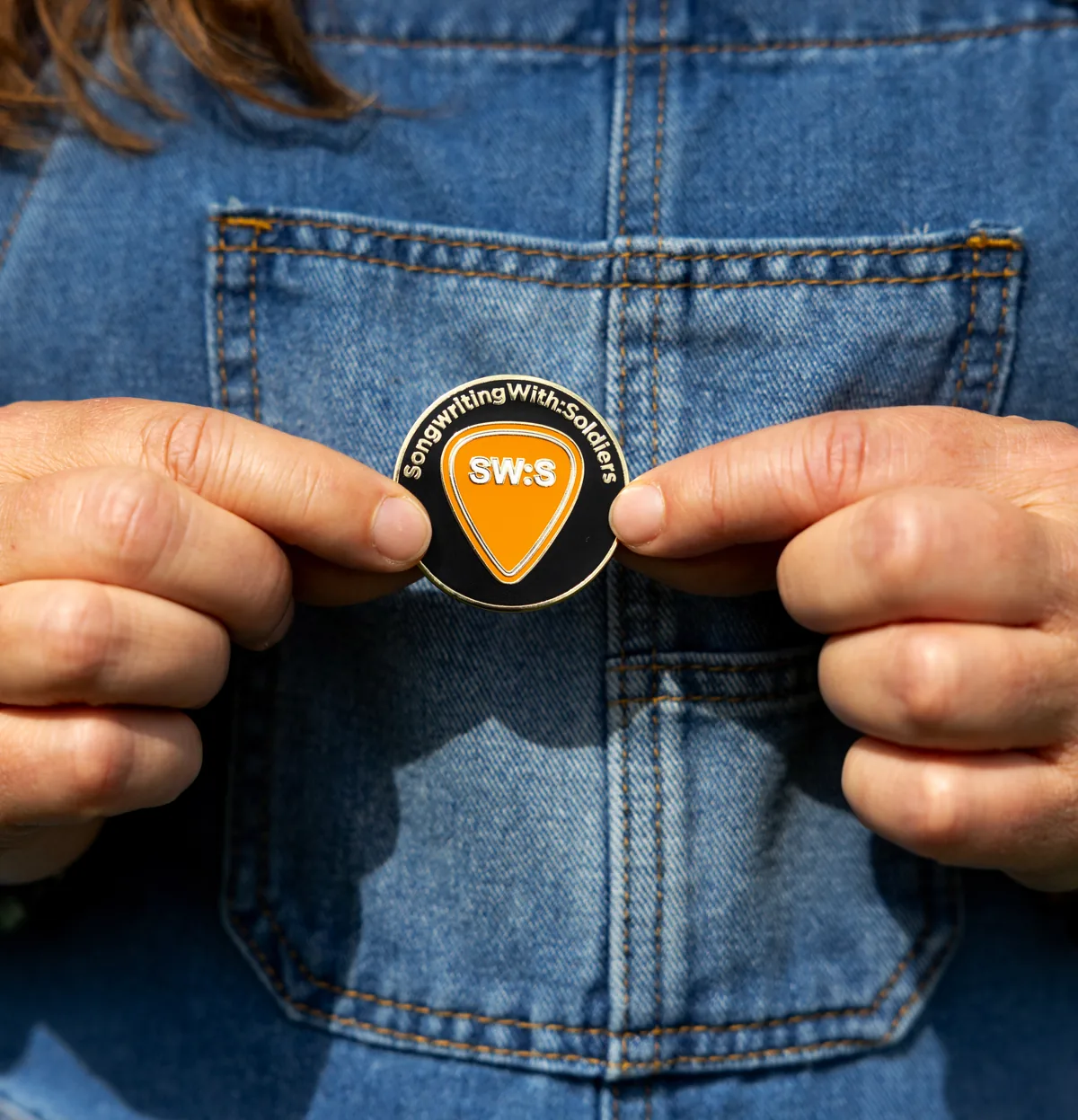 Hands holding the Songwriting with Soldiers coin against a denim jacket